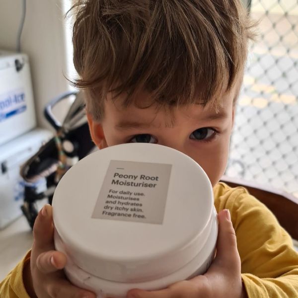 young boy holding tub of peony root moisturiser for dry itchy skin